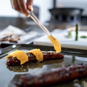 Chef garnishing grilled meat with orange slices in a modern kitchen